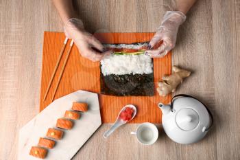 Woman making tasty sushi rolls at table�