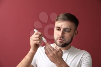Diabetic man taking blood sample with lancet pen on color background�