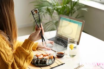 Woman eating tasty sushi rolls at home�