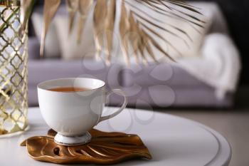 Cup of tea with tropical leaf on table in room�