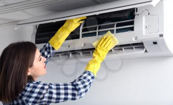Young woman cleaning air conditioner at home�