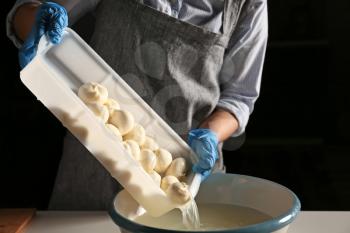 Woman preparing tasty cheese on dark background�