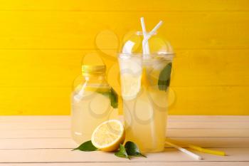 Bottle and plastic cup of fresh lemonade on table�