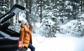 Young woman with hot drink near car at winter resort�