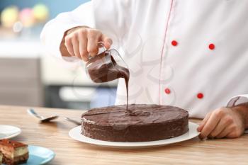 Male confectioner decorating tasty chocolate cake in kitchen, closeup�