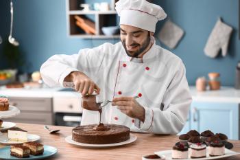 Male confectioner decorating tasty chocolate cake in kitchen�
