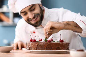 Male confectioner decorating tasty chocolate cake in kitchen�