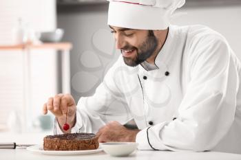 Male confectioner decorating tasty chocolate cake in kitchen�