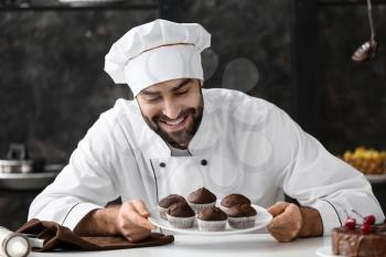 Male confectioner with tasty chocolate muffins in kitchen�