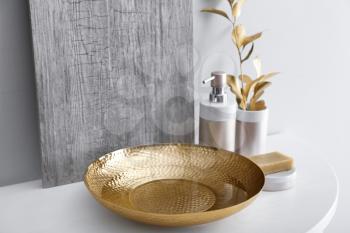 Golden bowl with water and cosmetics on table in bathroom�