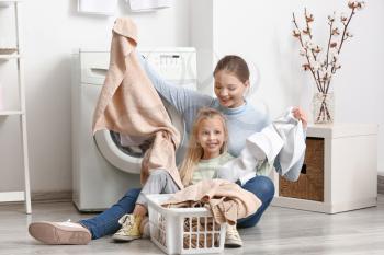 Young woman and her little daughter doing laundry at home�