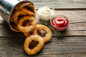 Overturned bucket with tasty onion rings and sauces on wooden table�