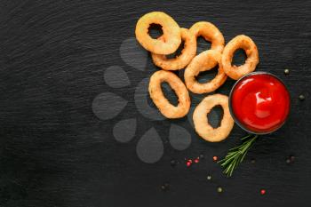 Tasty onion rings and tomato sauce on dark background�