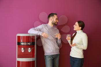 Man and woman drinking water from cooler against color background�