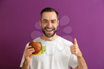 Man with tasty burger showing thumb-up on color background�