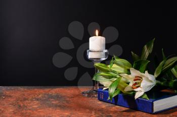 Burning candle, Bible and flowers on table against black background�