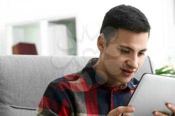 Young man with hearing aid using tablet computer at home�