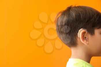 Little boy with hearing aid on color background�