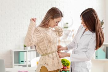Nutritionist measuring waist of young woman in clinic�
