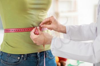 Nutritionist measuring waist of young woman in weight loss clinic, closeup�