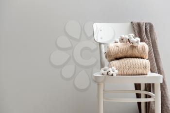 Knitted sweaters with cotton flowers on white chair against grey background�