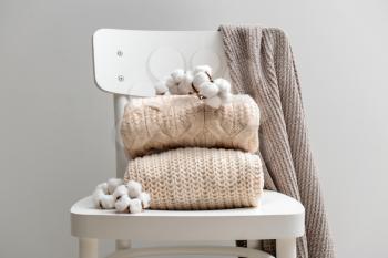 Knitted sweaters with cotton flowers on white chair against grey background�