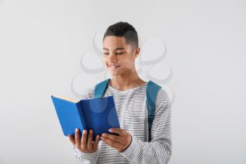 Portrait of African-American teenage boy with book on grey background�