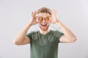 Funny young man with tasty cookies on light background�