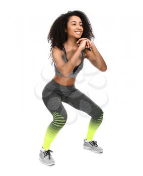 Sporty African-American woman doing squats on white background�