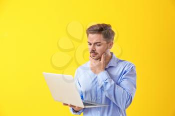 Thoughtful male programmer with laptop on color background�