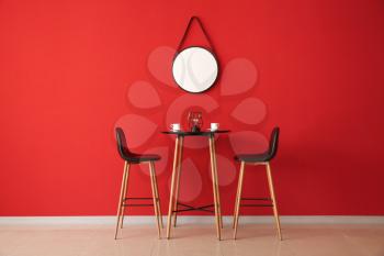 Table and chairs near color wall with mirror�
