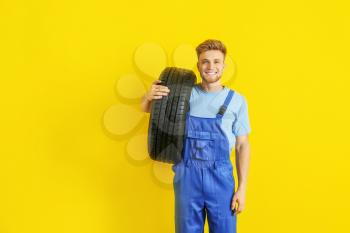 Young male mechanic with car tire on color background�
