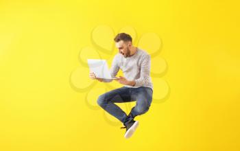 Jumping young man with laptop on color background�