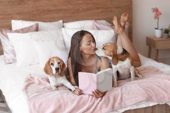 Young woman with cute dogs reading book on bed at home�