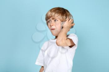 Cute little boy talking by mobile phone on color background�