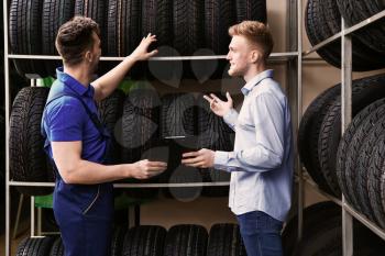 Seller helping man to choose tires in car store�