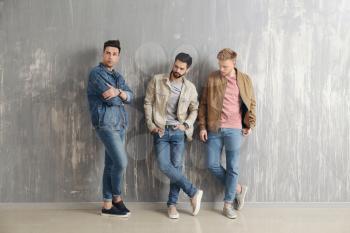 Fashionable young men near grey wall�