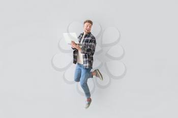Jumping young man with laptop on light background�