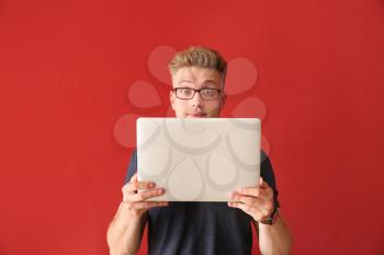Shocked young man with laptop on color background�