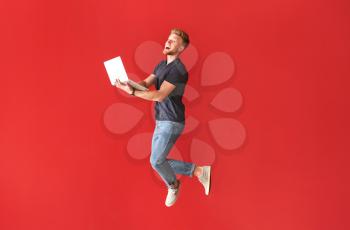 Jumping young man with laptop on color background�