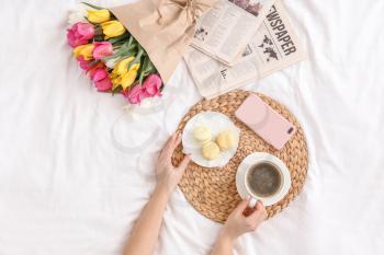 Woman drinking coffee and eating sweets on bed�