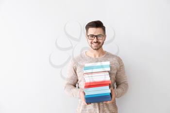 Handsome young man with books on light background�