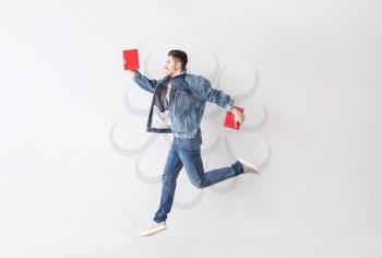Jumping young man with books on light background�