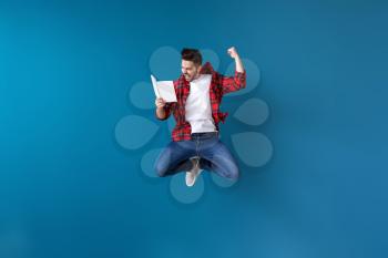 Jumping young man with book on color background�