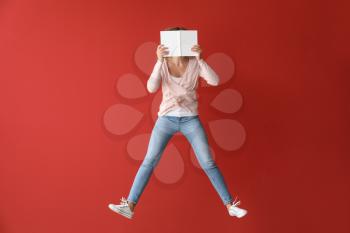 Jumping young woman with book on color background�