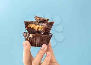 Female hand with chocolate butter cups on color background�