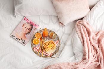 Tray with tasty breakfast and fashion magazine on bed�