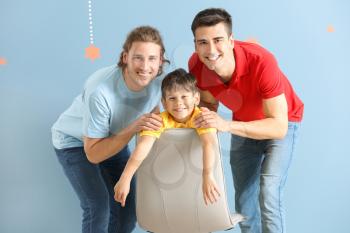 Happy gay couple with adopted child on color background�