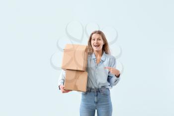 Young woman with cardboard boxes on light background�