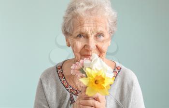 Portrait of senior woman with bouquet of flowers on grey background�